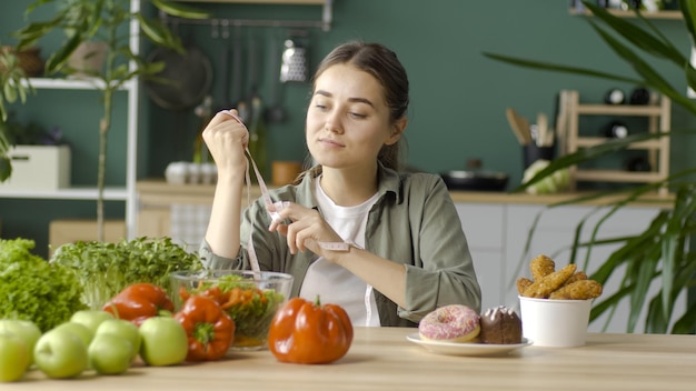 Una donna in cucina sceglie tra cibi biologici sani e ciambelle glassate