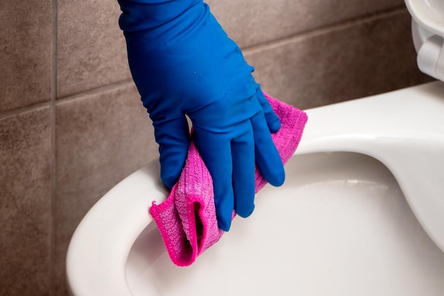Una donna in guanti di gomma pulisce la vaschetta del gabinetto con uno straccio