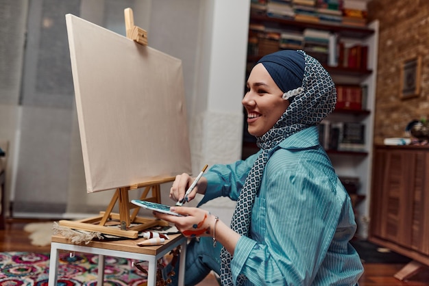 Una donna in hijab dipinge su tela con pennello e tempera