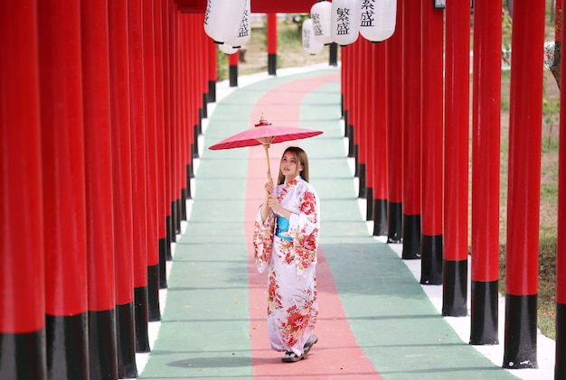 una donna in kimono con in mano un ombrello che entra nel santuario, nel giardino giapponese.