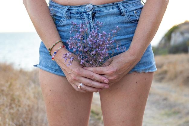 Una donna in pantaloncini corti sullo sfondo del mare e del campo tiene in mano dei fiori selvatici raccolti davanti al suo viaggio e turismo