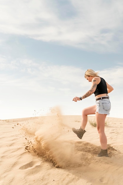 Una donna in pantaloncini nel deserto scava la sabbia con il piede, creando una nuvola di polvere