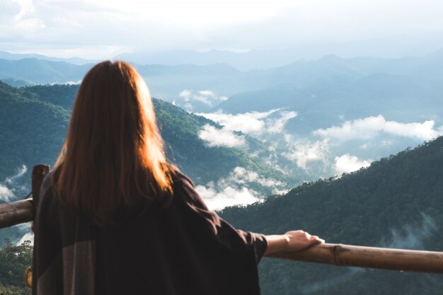 Una donna in piedi da sola sul balcone guardando le montagne in una giornata nebbiosa con cielo blu al mattino