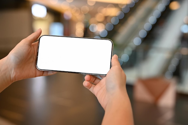 Una donna in possesso di un telefono cellulare con schermo bianco su sfondo sfocato centro commerciale