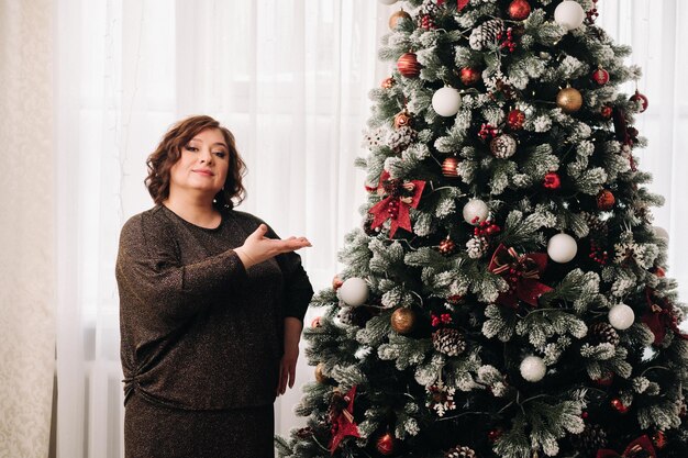 Una donna in un abito scuro in piedi accanto a un albero di Natale in un interno progettato per celebrare il Natale e il Capodanno