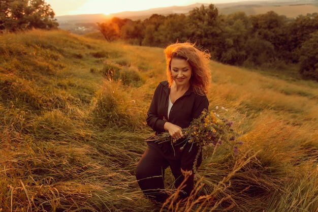 Una donna in un campo di erba alta tiene in mano un fiore.