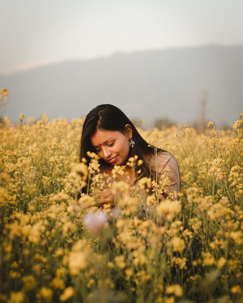 Una donna in un campo di fiori gialli con una montagna sullo sfondo.