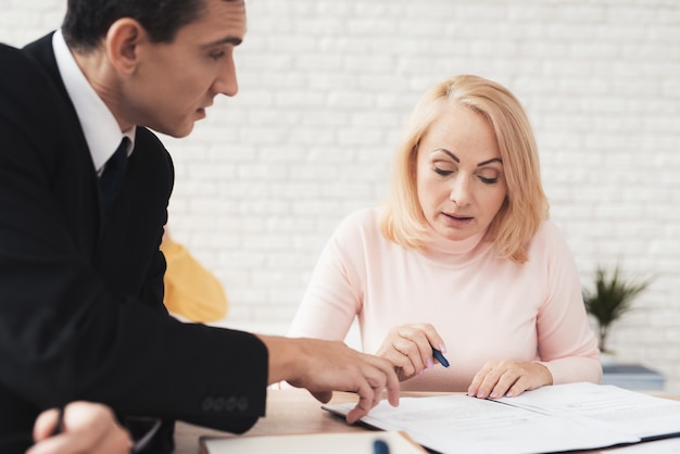 Una donna in un maglione rosa firma un contratto con un agente immobiliare.