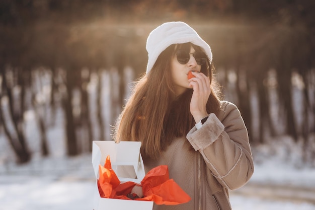 una donna in un parco invernale apre un regalo con un nastro rosso