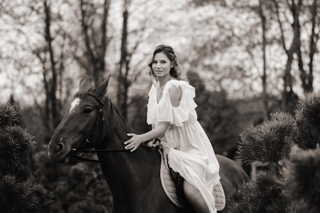 Una donna in un prendisole bianco a cavallo vicino a una fattoria foto in bianco e nero