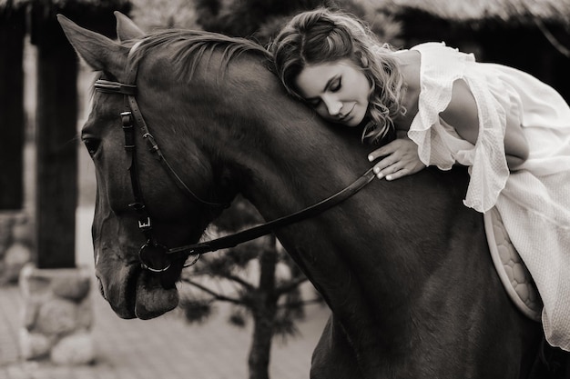 Una donna in un prendisole bianco a cavallo vicino a una fattoria foto in bianco e nero