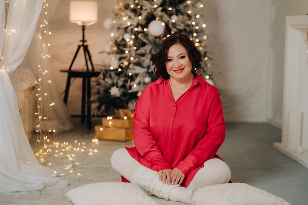 Una donna in una camicia rossa in una stanza decorata per l'atmosfera di Natale a casa di Capodanno