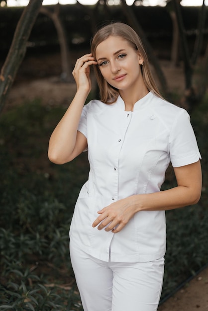 Una donna in uniforme bianca si trova di fronte a un albero e indossa un top bianco con sopra la parola spa.