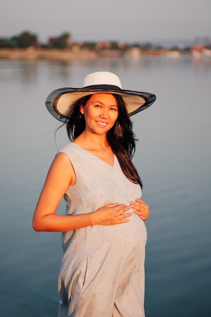 Una donna incinta al tramonto una donna incinta sorridente felice con un cappello di paglia e un vestito posa al tramo...