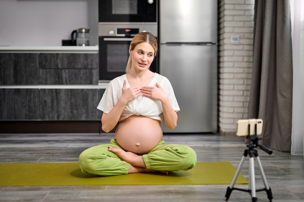 Una donna incinta amichevole si siede sul tappetino fitness registrando video su smartphone