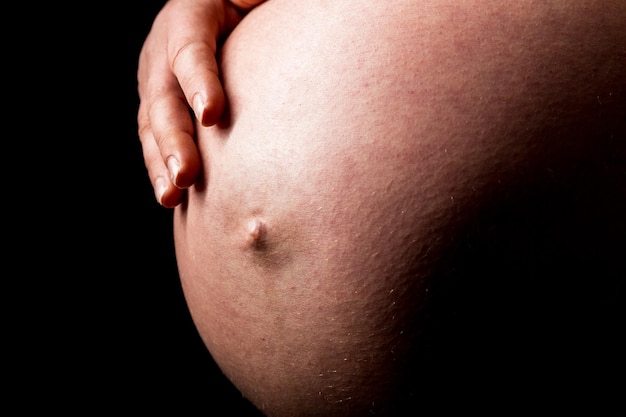 Una donna incinta che accarezza la sua pancia sul nero. Scattata in Studio con una 5D mark III.