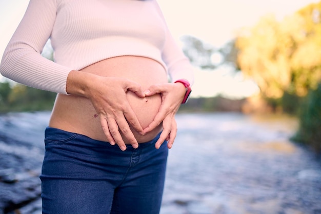 Una donna incinta che fa una forma del cuore con le mani sulla sua pancia