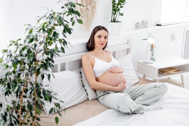 Una donna incinta con una grande pancia aperta su un letto a casa sogna di avere un bambino La futura mamma sta aspettando e preparando la nascita di un bambino in una luminosa camera da letto