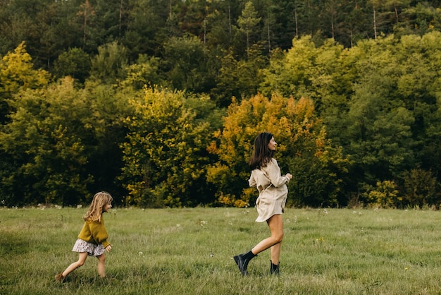 Una donna incinta e la sua bambina corrono in un campo con l'erba verde e trascorrono del tempo insieme