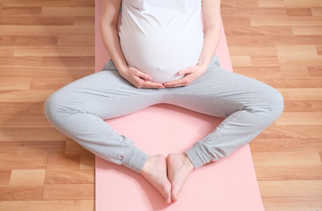 Una donna incinta è seduta su una stuoia di yoga. Concetto di cibo e stile di vita sano. Pancia da vicino