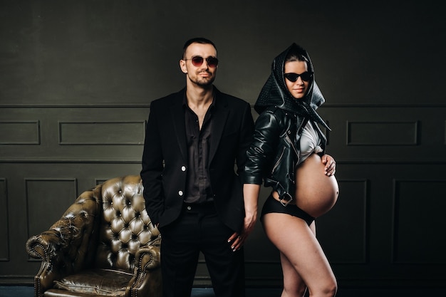 Una donna incinta in abiti neri e un velo e un uomo in abito in uno studio su uno sfondo scuro