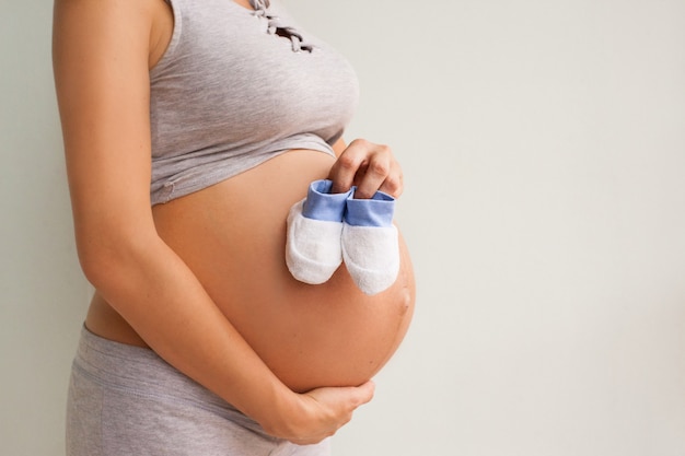 Una donna incinta tiene un paio di scarpe per bambini davanti alla sua pancia incinta.