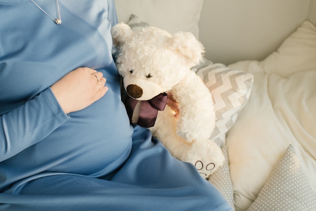 Una donna incinta tiene una mano sul suo stomaco e accanto ad essa un orsetto di peluche