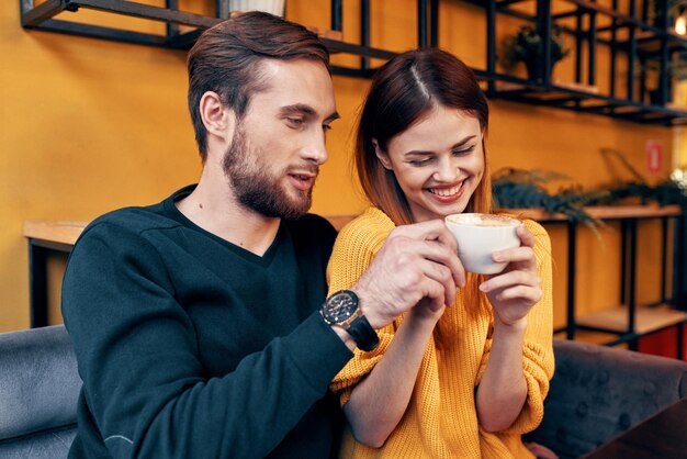 Una donna innamorata di una tazza di caffè e un uomo felice a un tavolo in una comunicazione di amici interni di un caffè