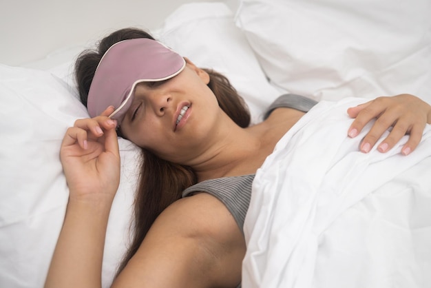 Una donna insoddisfatta con una maschera da sonno soffre di insonnia sdraiata sul letto con una coperta di neve nella stanza