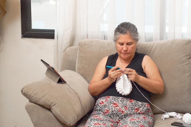 Una donna latina matura lavora a maglia a casa imparando l'artigianato online