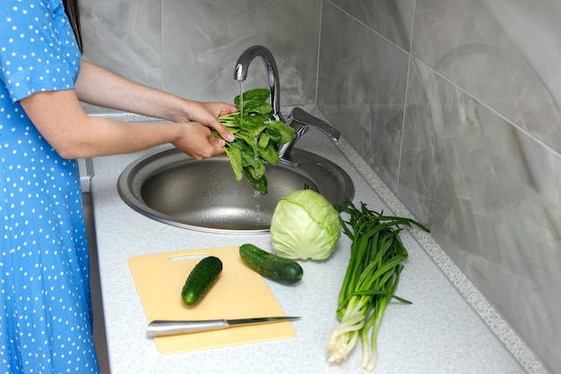 Una donna lava gli spinaci in un lavandino in cucina per un'insalata