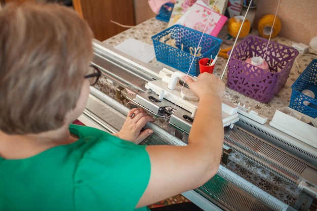 Una donna lavora a maglia su una macchina per maglieria, lavorando con le sue mani