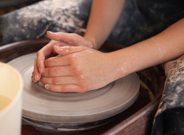 Una donna lavora su un tornio da vasaio Le mani formano una tazza di argilla bagnata su un tornio da vasaio Concetto artistico