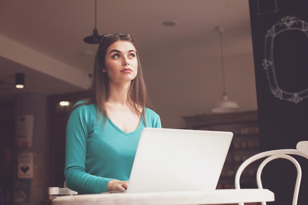 Una donna-libera professionista con gli occhiali neri sta lavorando con il suo laptop grigio al tavolo di legno e sta pensando a qualcosa