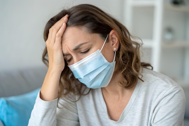 Una donna malata con mal di testa indossava una maschera e si metteva una mano sulla testa