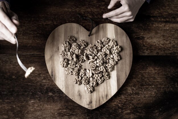 Una donna mangia noci da un vassoio di legno a forma di cuore Sfondo in legno Noci sgusciate Mangiare sano