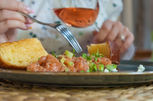 Una donna mangia tartare di salmone con vino rosato