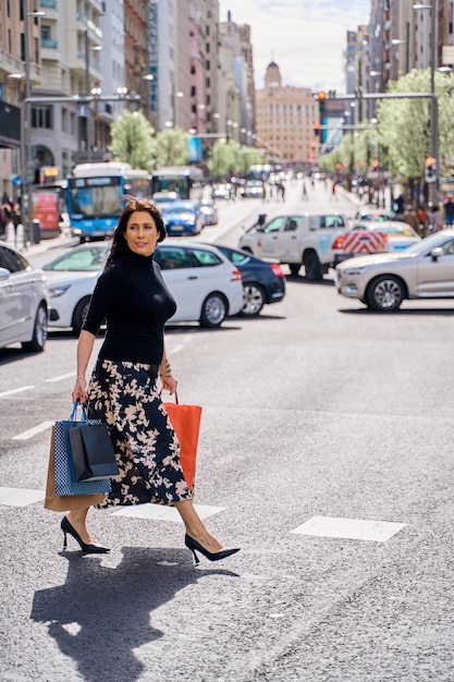 una donna matura che si diverte a fare shopping in città attraversa la strada con delle borse per la spesa