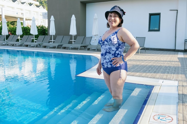 Una donna matura in costume da bagno e panama scende le scale fino alla piscina
