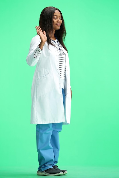 Una donna medico su uno sfondo verde a tutta altezza agitando la mano