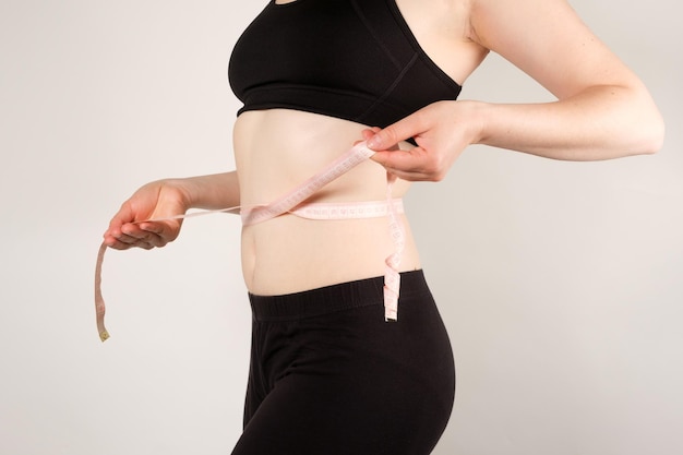 Una donna misura la circonferenza dell'addome con un primo piano del nastro di centimetro Concetto dimagrante