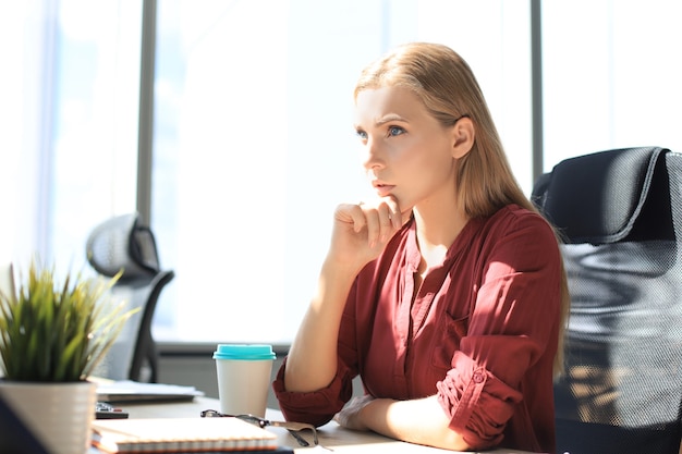 Una donna moderna e concentrata tiene la mano sul mento e pensa agli affari mentre lavora in ufficio.