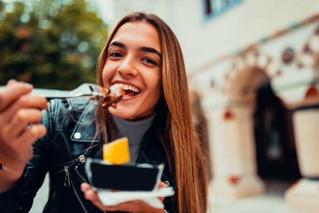 Una donna moderna si siede nel parco in una pausa dal college e mangia poffertjes freschi Messa a fuoco selettiva