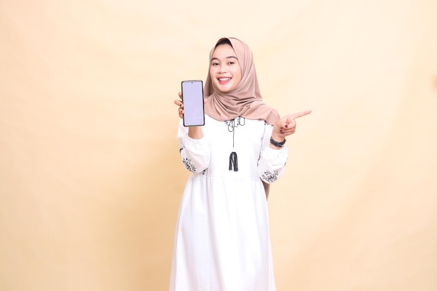 una donna musulmana adulta indonesiana che indossa un hijab con un sorriso allegro mostra uno schermo di cellulare ga