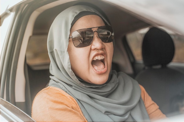Una donna musulmana asiatica che guida un'auto si arrabbia e si arrabbia per il traffico urlando un gesto maleducato dalla sua auto