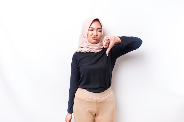 Una donna musulmana asiatica delusa che indossa un hijab dà il pollice verso il basso gesto della mano di disapprovazione isolato da sfondo bianco