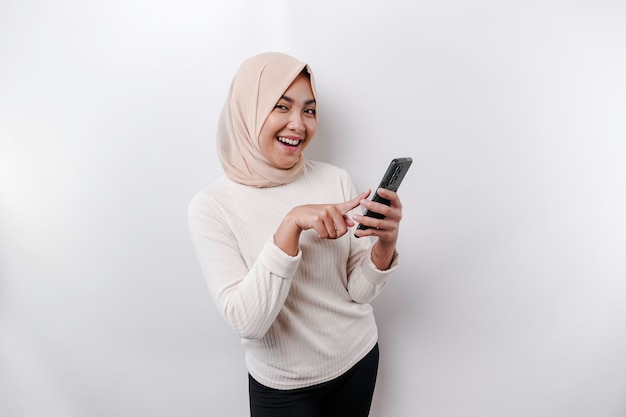 Una donna musulmana asiatica felice che indossa un velo che tiene il suo telefono isolato da sfondo bianco