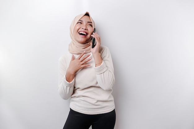 Una donna musulmana asiatica felice che indossa un velo che tiene il suo telefono isolato da sfondo bianco