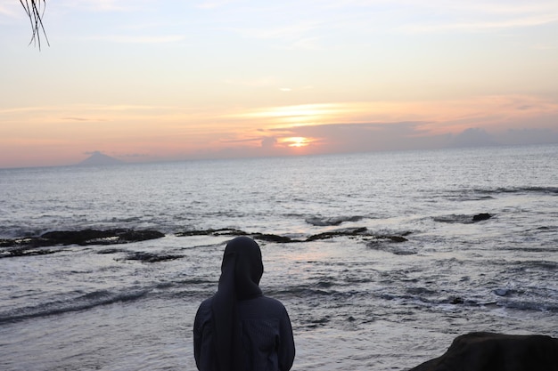 Una donna musulmana che guarda il tramonto sulla spiaggia.