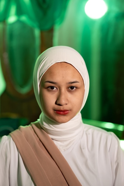 Una donna musulmana con un velo bianco e abiti bianchi è seduta al centro di una stanza verde